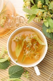 Photo of Fresh linden tea in cup, teapot and flowers on white wooden table, flat lay