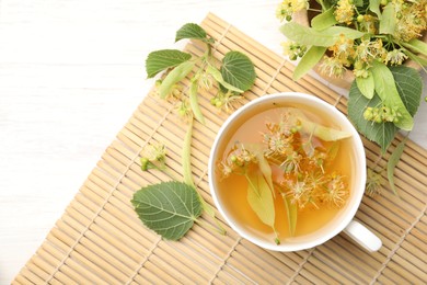 Photo of Fresh linden tea in cup and flowers on white wooden table, flat lay. Space for text