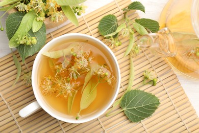 Photo of Fresh linden tea in cup, teapot and flowers on white wooden table, flat lay