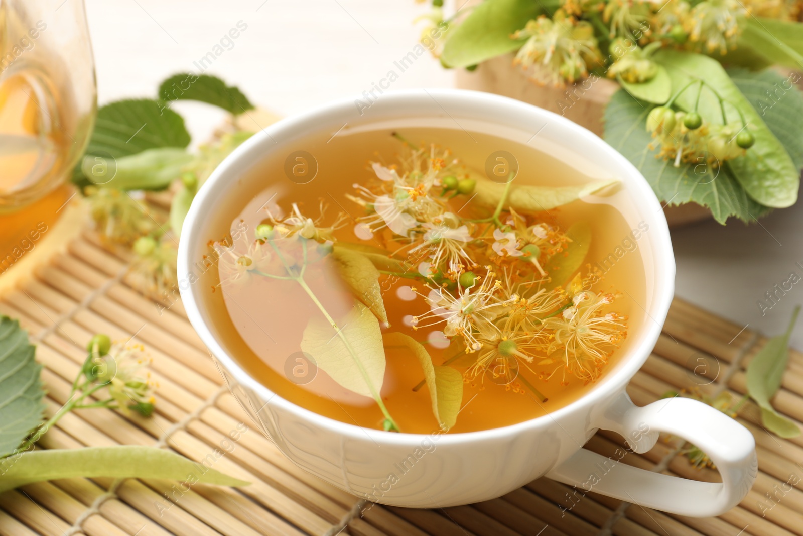 Fresh linden tea in cup, teapot and flowers on white table, closeup Photo of Fresh linden tea in cup, teapot and flowers on white table, closeup