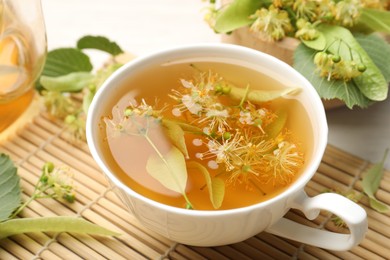Photo of Fresh linden tea in cup, teapot and flowers on white table, closeup