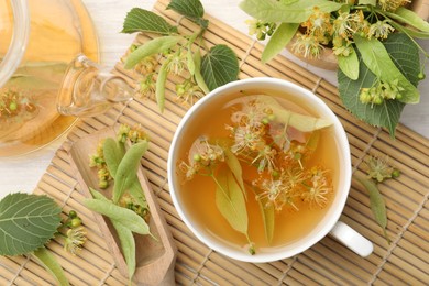 Photo of Fresh linden tea in cup, teapot and flowers on white wooden table, flat lay