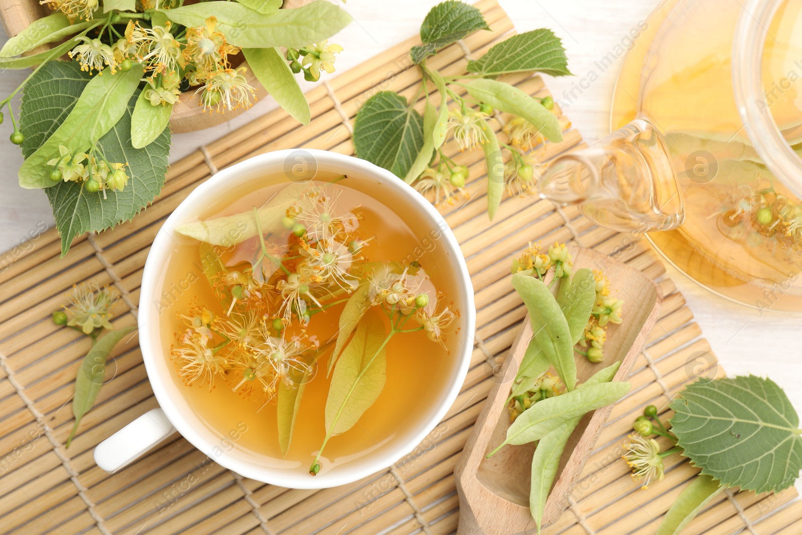 Fresh linden tea in cup, teapot and flowers on white wooden table, flat lay Photo of Fresh linden tea in cup, teapot and flowers on white wooden table, flat lay