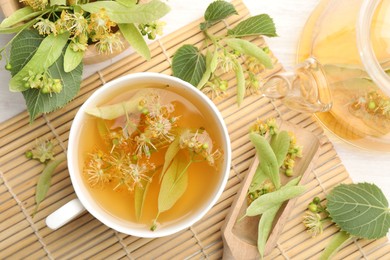 Photo of Fresh linden tea in cup, teapot and flowers on white wooden table, flat lay