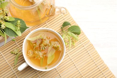 Photo of Fresh linden tea in cup, teapot and flowers on white wooden table, flat lay. Space for text