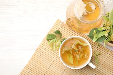 Photo of Fresh linden tea in cup, teapot and flowers on white wooden table, flat lay. Space for text
