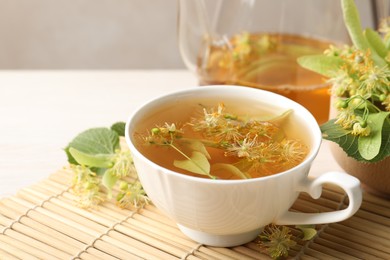 Photo of Fresh linden tea in cup, teapot and flowers on white table, closeup. Space for text