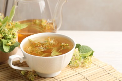 Photo of Fresh linden tea in cup, teapot and flowers on white table, closeup. Space for text