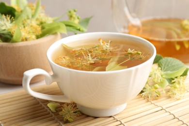 Photo of Fresh linden tea in cup, teapot and flowers on table, closeup