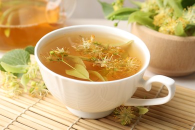 Photo of Fresh linden tea in cup, teapot and flowers on table, closeup