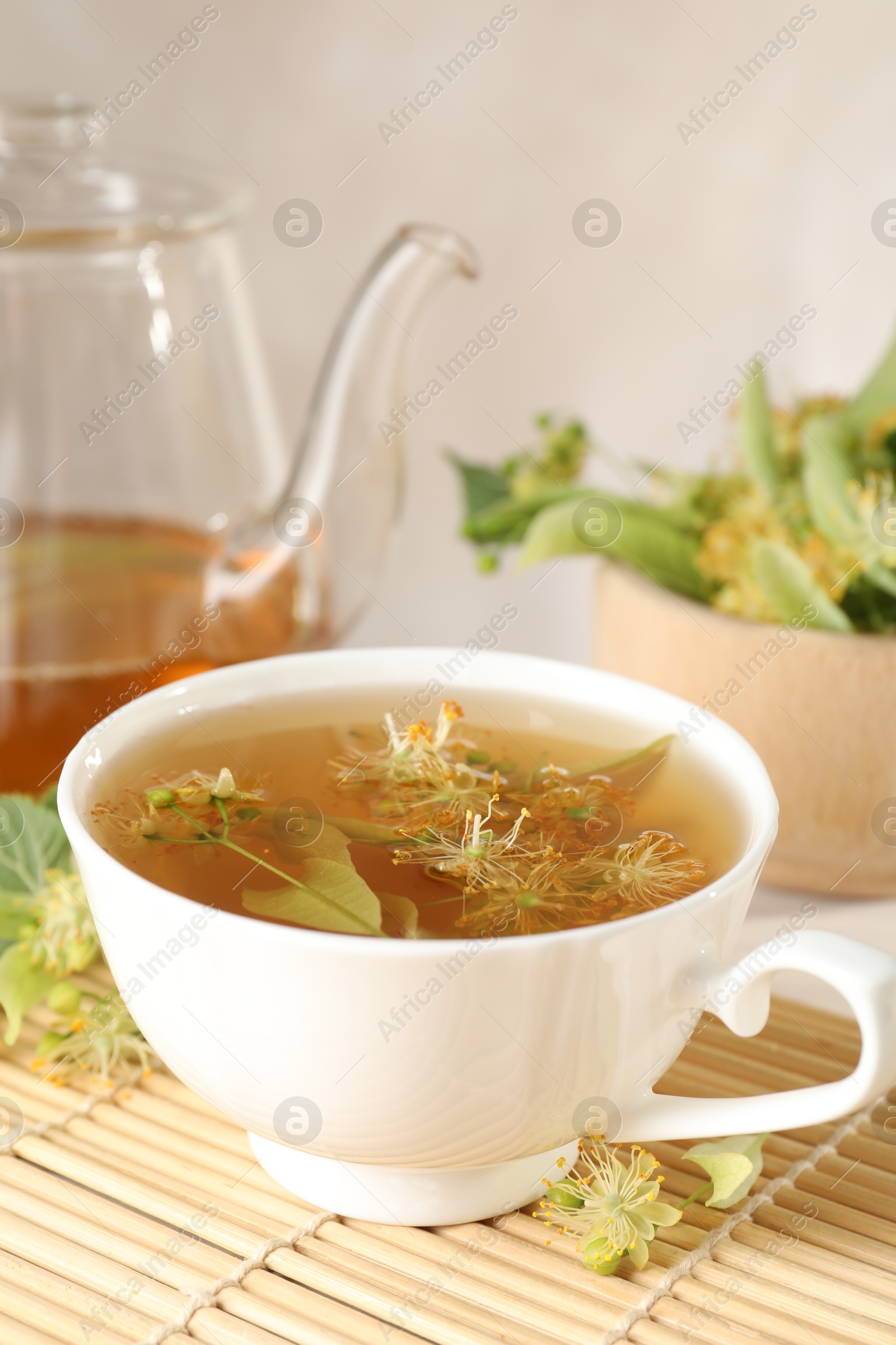 Fresh linden tea in cup, teapot and flowers on table, closeup Photo of Fresh linden tea in cup, teapot and flowers on table, closeup