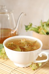Photo of Fresh linden tea in cup, teapot and flowers on table, closeup