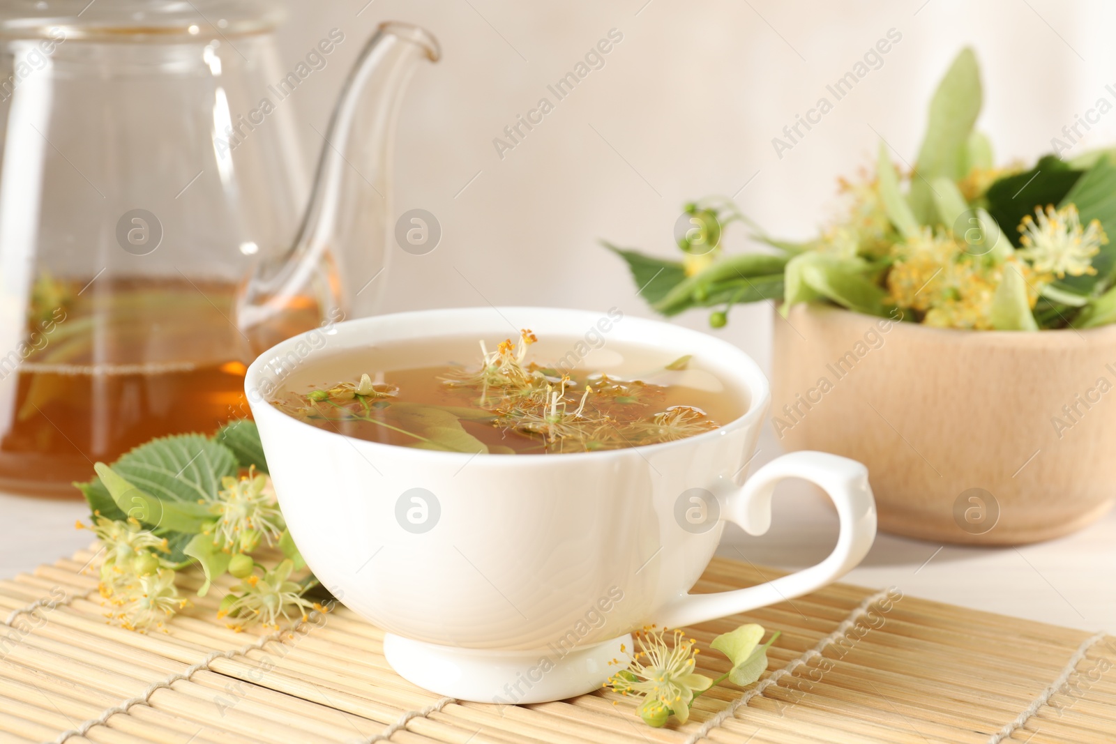 Fresh linden tea in cup, teapot and flowers on white table, closeup Photo of Fresh linden tea in cup, teapot and flowers on white table, closeup