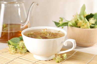 Photo of Fresh linden tea in cup, teapot and flowers on white table, closeup