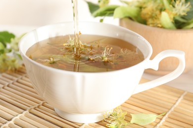 Photo of Pouring fresh linden tea into cup and flowers on table, closeup