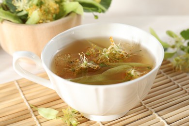 Photo of Fresh linden tea in cup and flowers on table, closeup