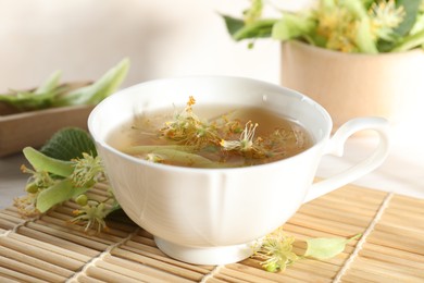 Photo of Fresh linden tea in cup and flowers on white table, closeup