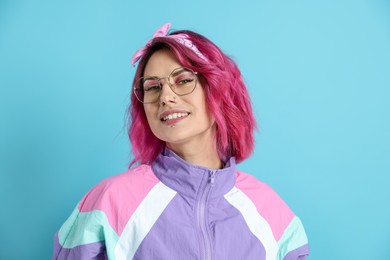 Photo of Beautiful woman with pink dyed hair in glasses on light blue background
