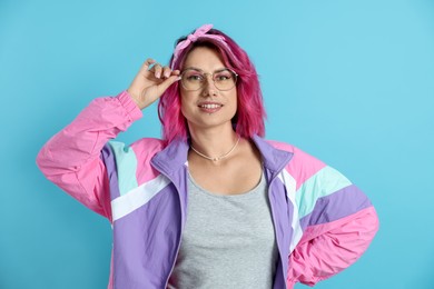 Photo of Beautiful woman with pink dyed hair in glasses on light blue background