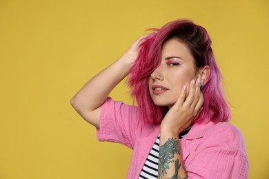 Photo of Beautiful woman with pink dyed hair on yellow background, space for text
