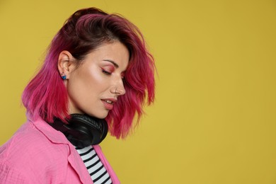 Photo of Beautiful woman with pink dyed hair and headphones on yellow background, space for text
