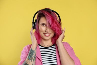 Photo of Beautiful woman with pink dyed hair listening to music on yellow background
