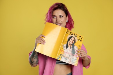Photo of Beautiful woman with pink dyed hair holding fashion magazine on yellow background