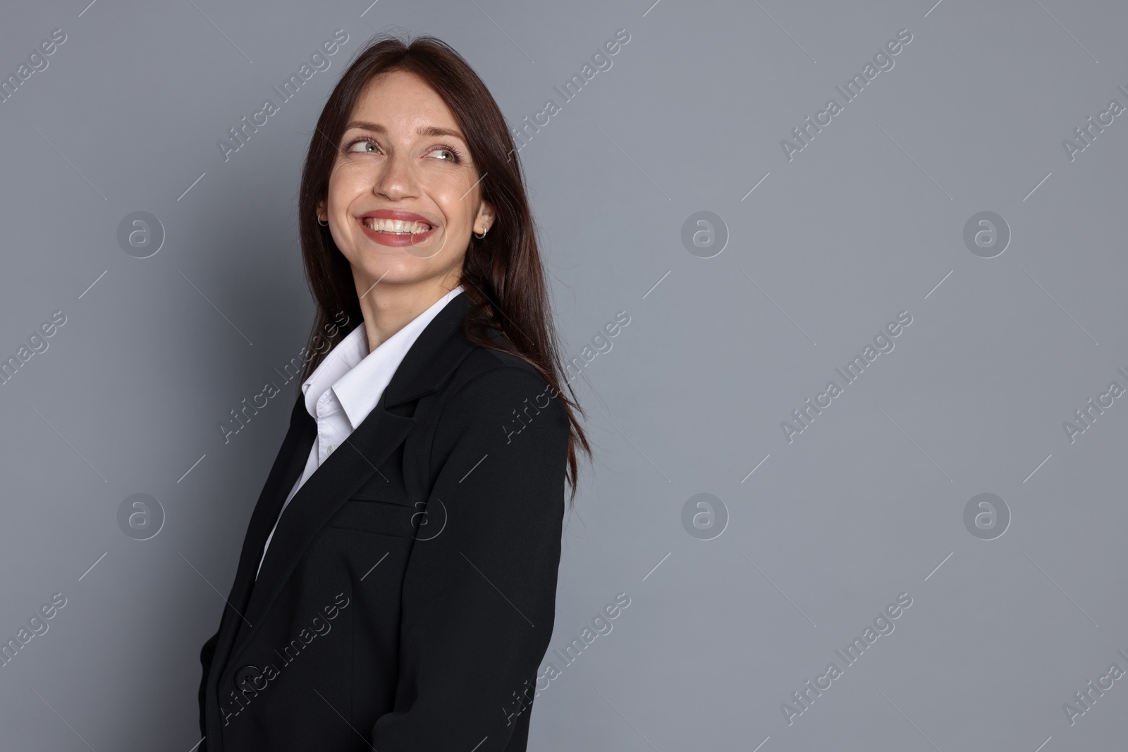 Happy woman in suit on grey background, space for text Photo of Happy woman in suit on grey background, space for text