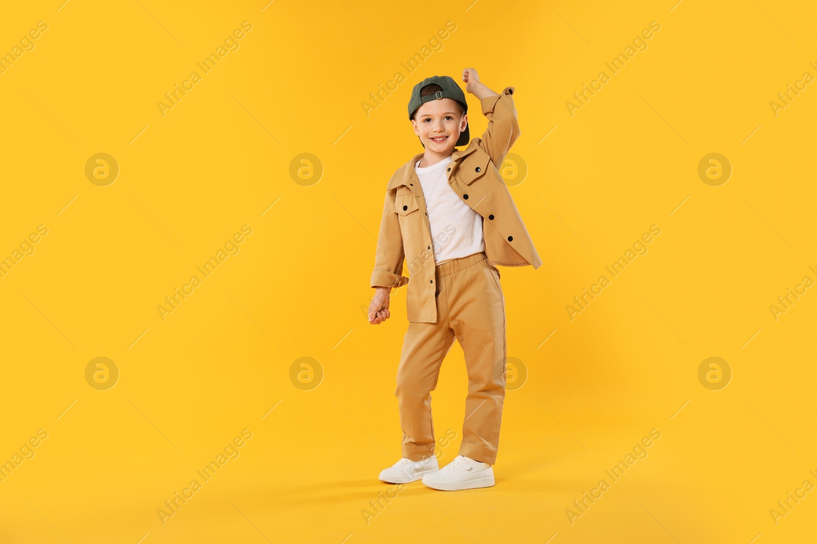 Happy little boy in baseball hat dancing on orange background Photo of Happy little boy in baseball hat dancing on orange background