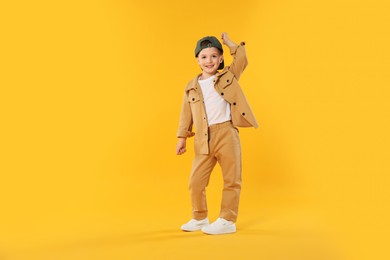 Photo of Happy little boy in baseball hat dancing on orange background