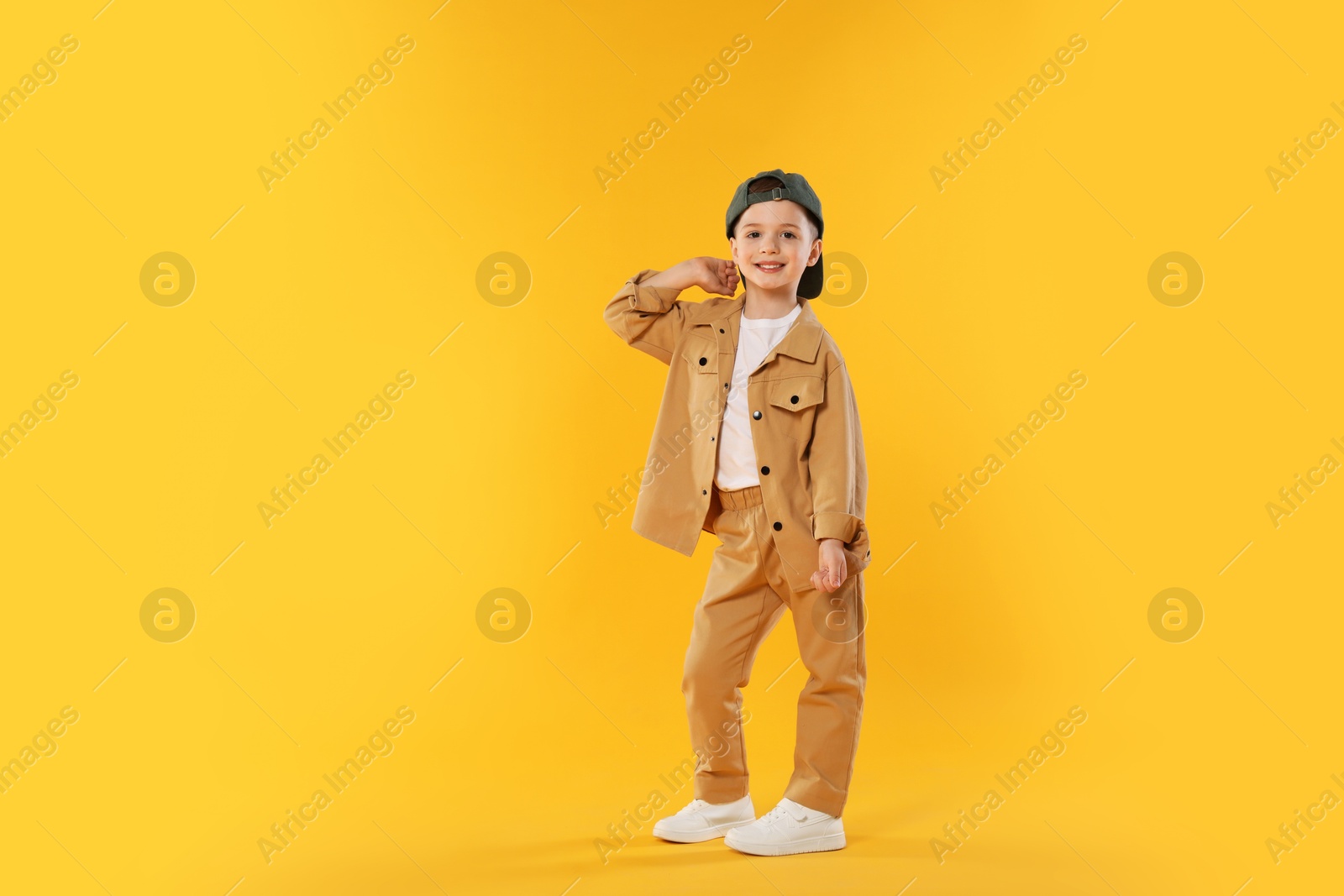 Happy little boy in baseball hat dancing on orange background Photo of Happy little boy in baseball hat dancing on orange background