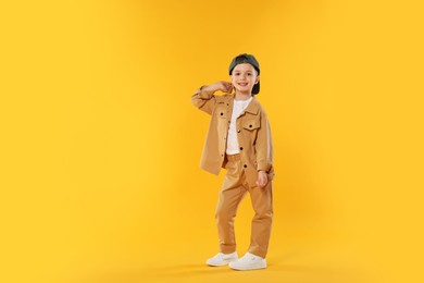 Photo of Happy little boy in baseball hat dancing on orange background