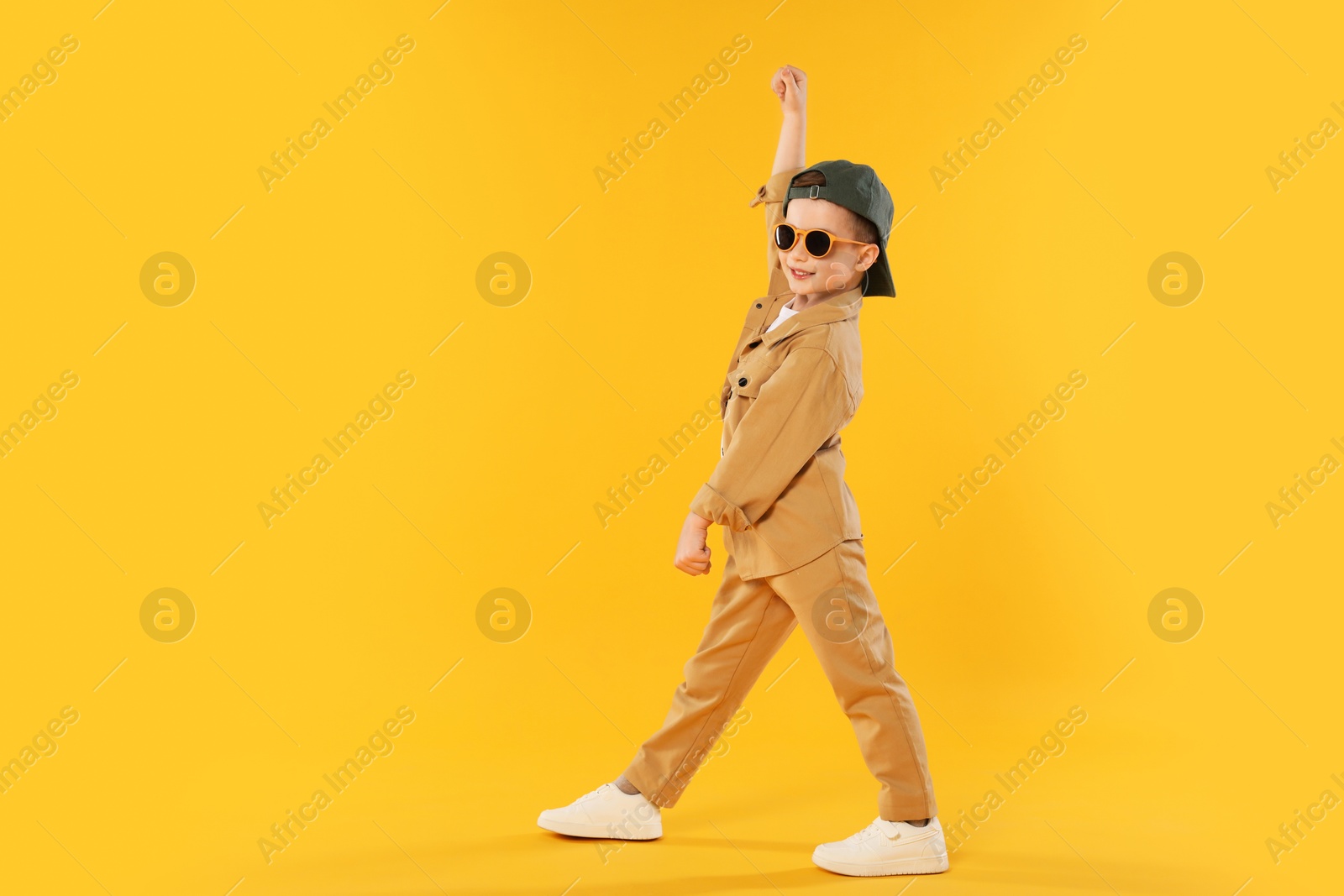 Happy little boy in sunglasses and baseball hat dancing on orange background. Space for text Photo of Happy little boy in sunglasses and baseball hat dancing on orange background. Space for text