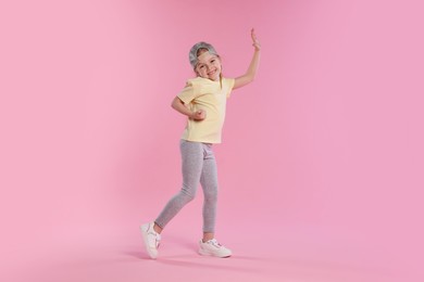 Photo of Cute little girl dancing on pink background