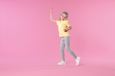 Photo of Cute little girl dancing on pink background