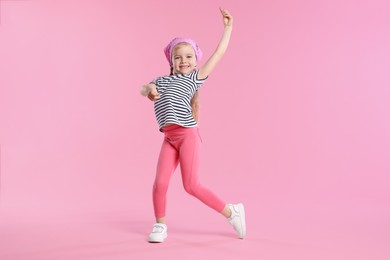 Photo of Cute little girl dancing on pink background