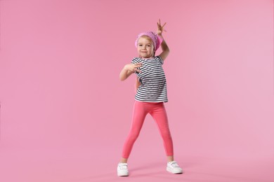 Photo of Cute little girl dancing on pink background