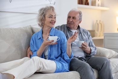 Photo of Lovely senior couple enjoying hot drinks on sofa at home