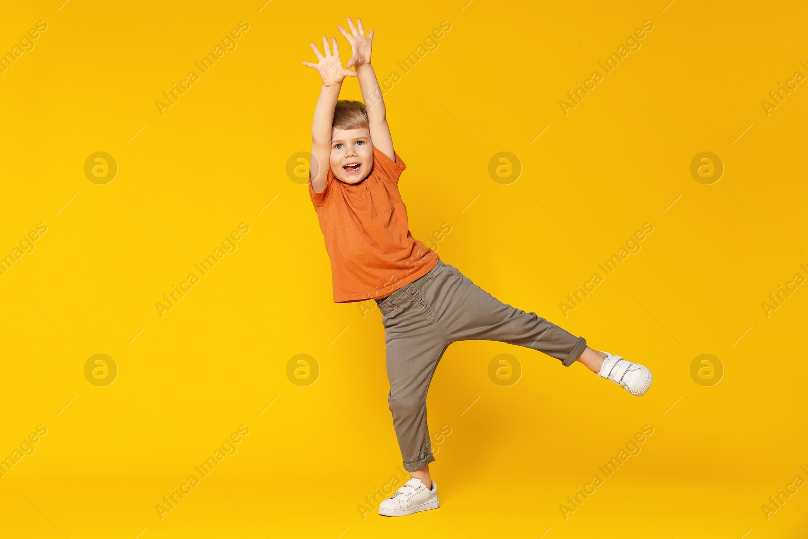 Happy little boy dancing on orange background, space for text Photo of Happy little boy dancing on orange background, space for text
