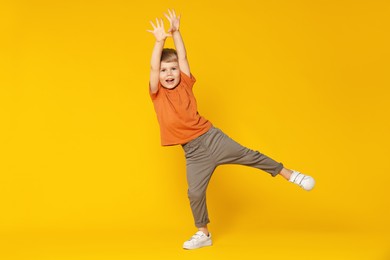 Photo of Happy little boy dancing on orange background, space for text