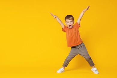 Photo of Happy little boy dancing on orange background, space for text