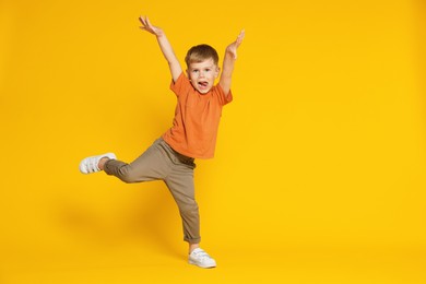 Photo of Happy little boy dancing on orange background, space for text