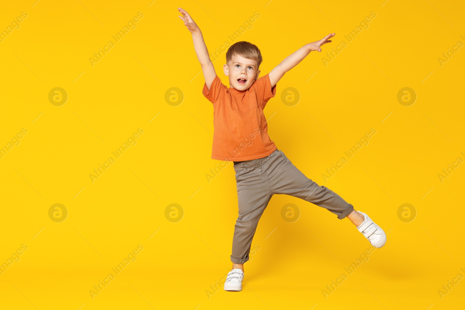 Happy little boy dancing on orange background, space for text Photo of Happy little boy dancing on orange background, space for text