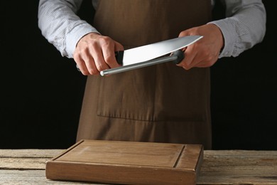 Photo of Man sharpening knife with sharpener on wooden table, closeup