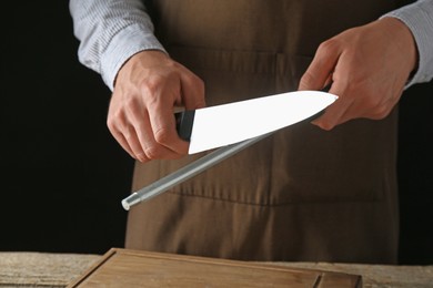 Photo of Man sharpening knife with sharpener on wooden table, closeup