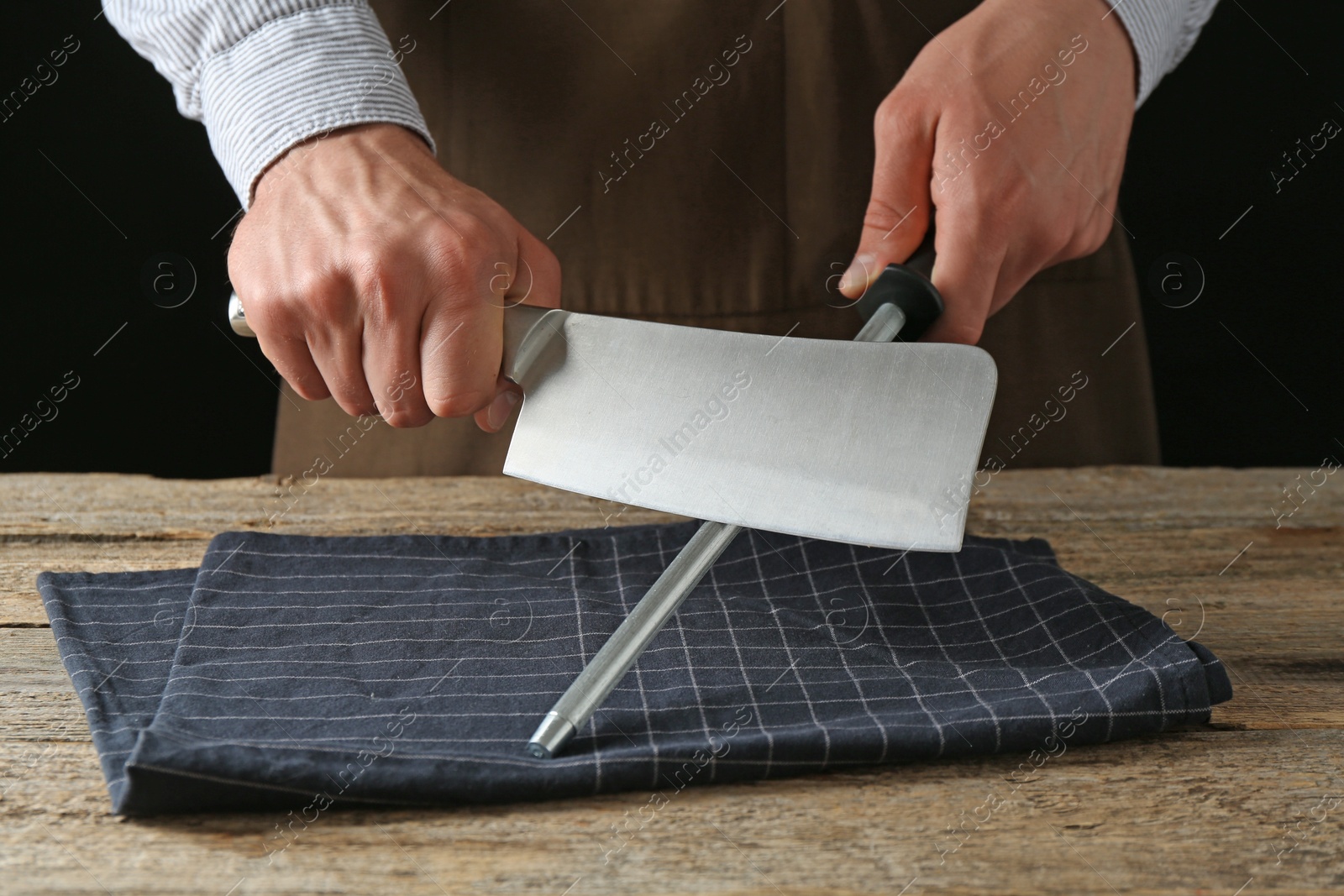 Man sharpening knife with sharpener on wooden table, closeup Photo of Man sharpening knife with sharpener on wooden table, closeup