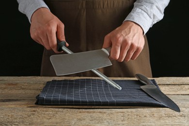 Photo of Man sharpening knife with sharpener on wooden table, closeup