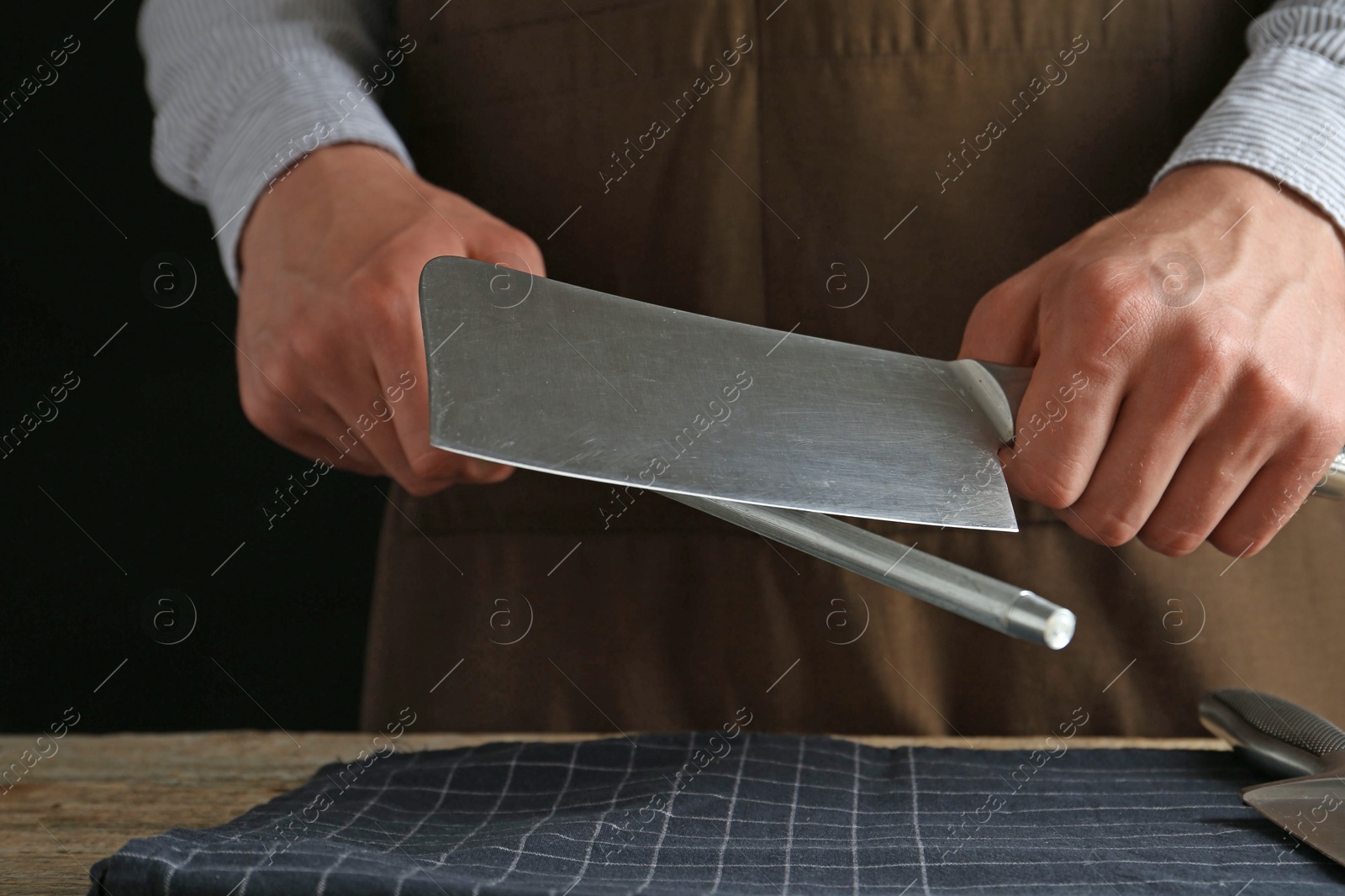 Man sharpening knife with sharpener on wooden table, closeup Photo of Man sharpening knife with sharpener on wooden table, closeup
