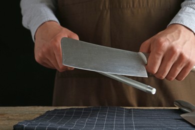 Photo of Man sharpening knife with sharpener on wooden table, closeup