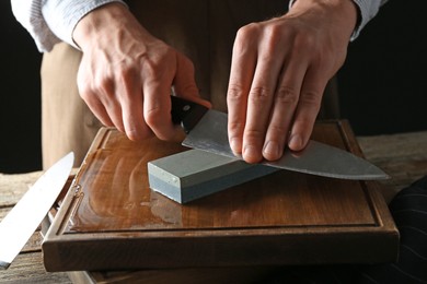 Photo of Man sharpening knife with sharpener on wooden table, closeup